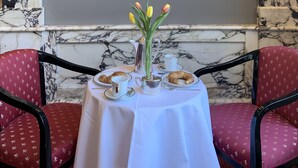 A dining area with a table set for two, a framed portrait on the wall, and a vase of tulips.