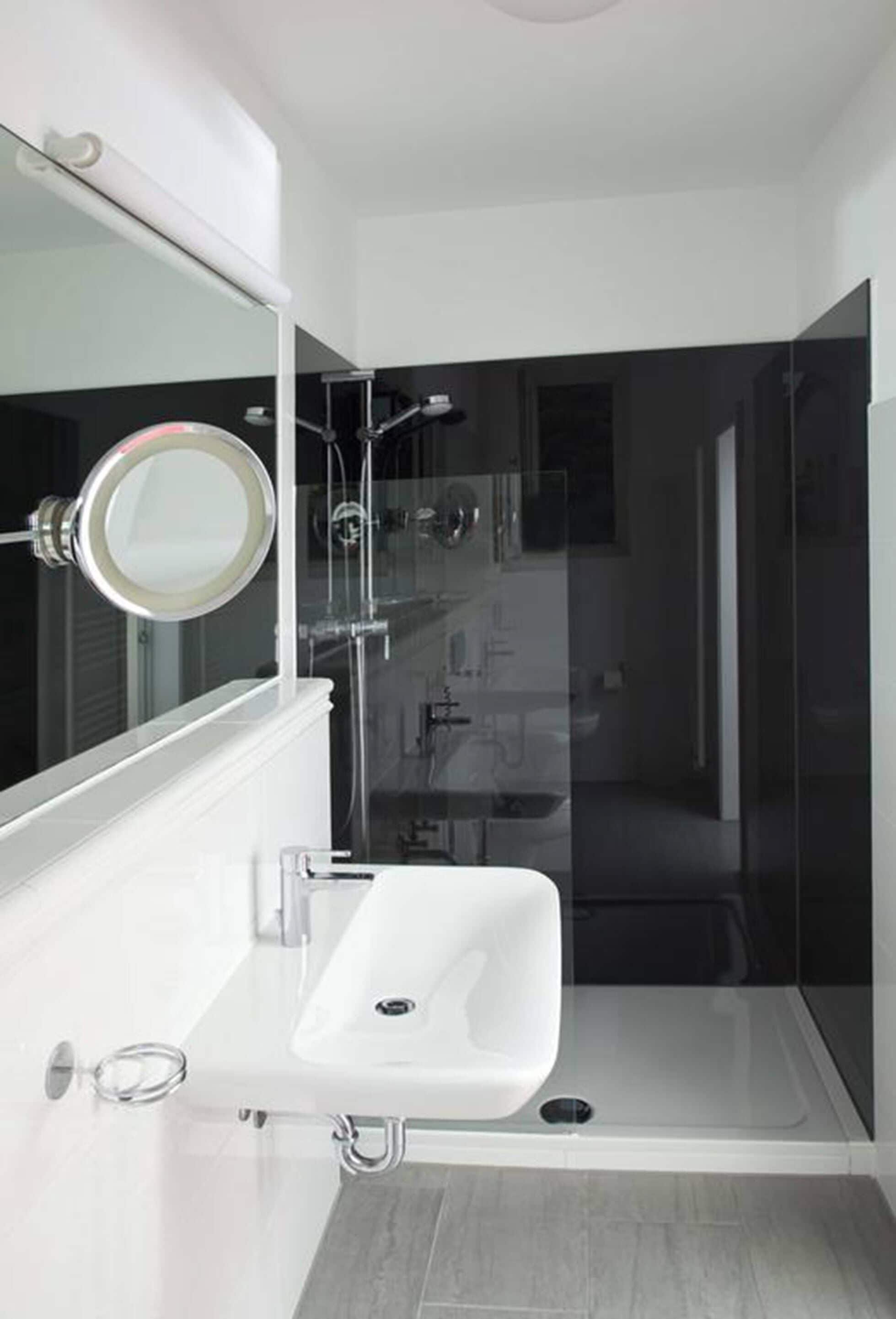 Un baño moderno con ducha de vidrio, un lavabo blanco y un espejo encima.