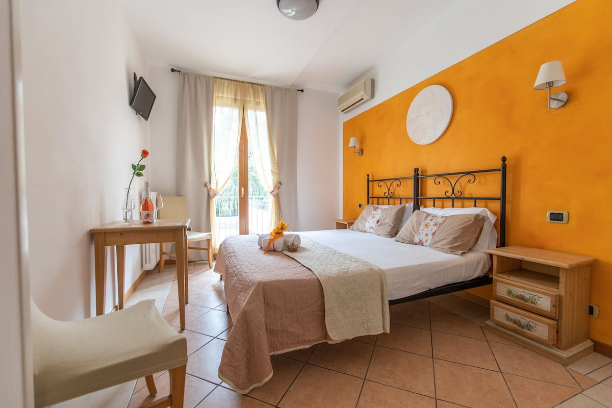 Un dormitorio con cama, mesita de noche, silla y ventana con cortinas.