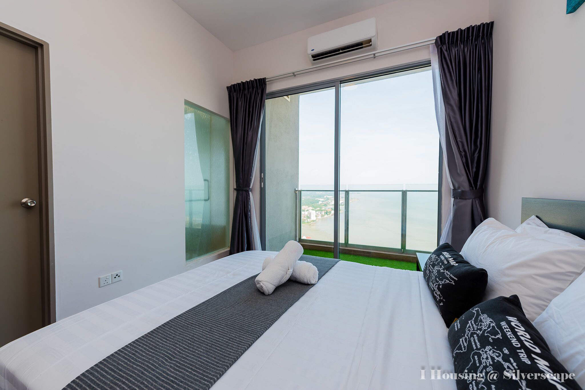 Ein Hotelzimmer mit einem großen Bett, Meerblick durch eine Schiebeglasdoor und einem mit Vorhängen versehenen Fenster.