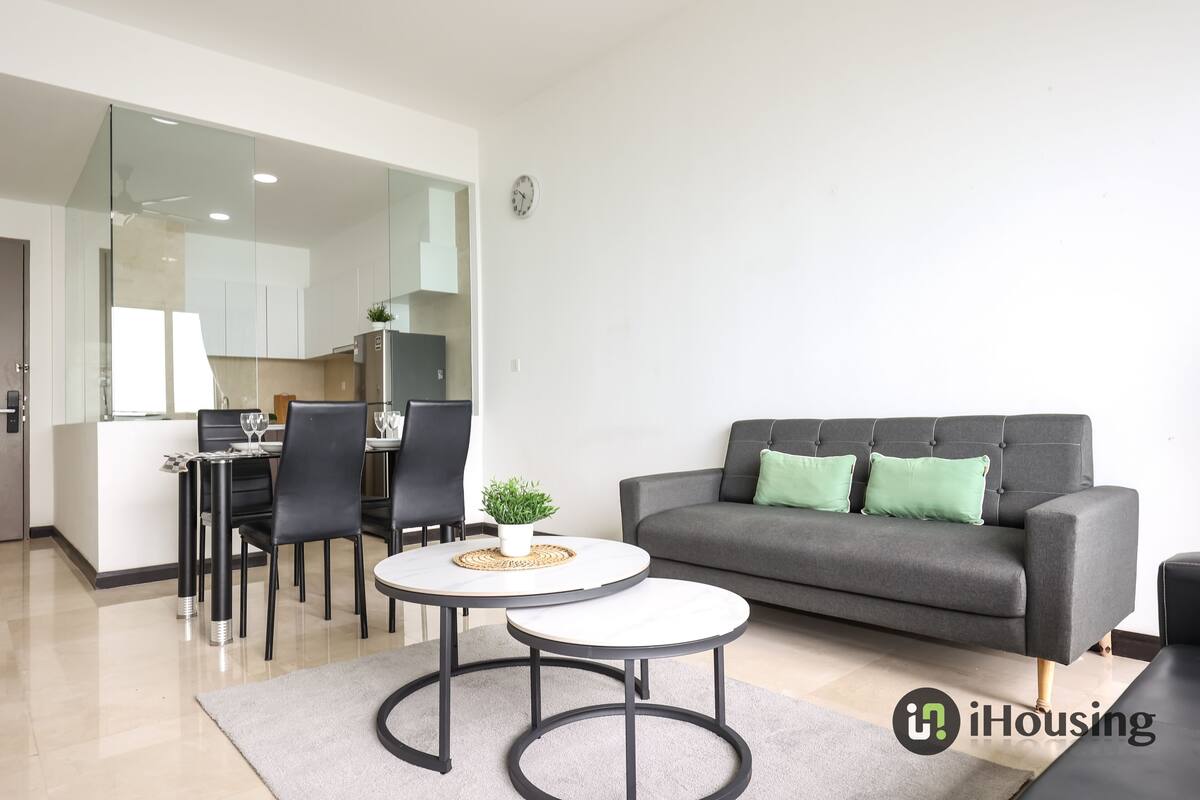 A modern living room with a grey sofa, two round tables, and a dining area with chairs and a small plant.