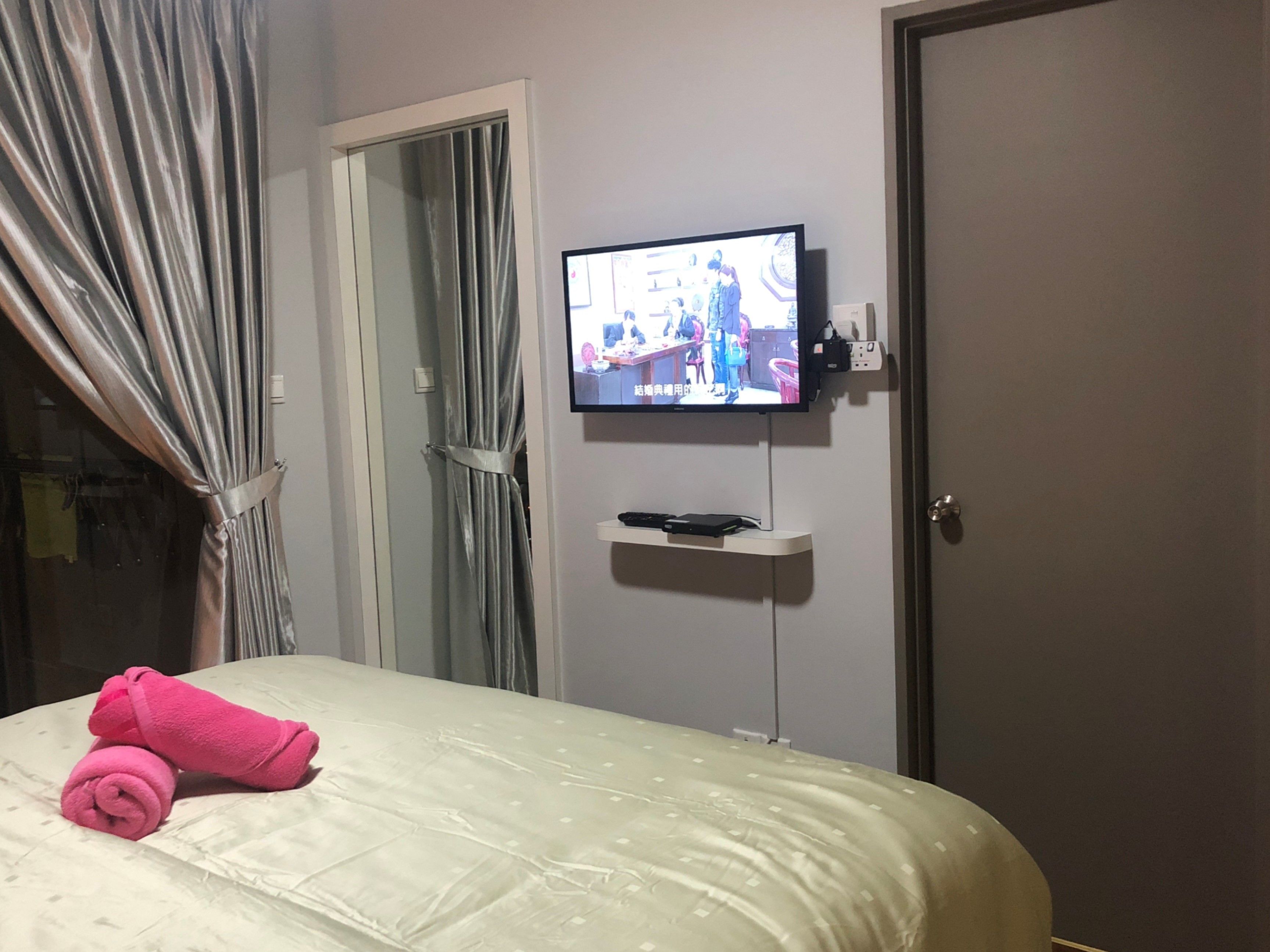 Hotellihuone, jossa on sänky, seinälle asennettu televisio ja verhoilla varustettu ovi.