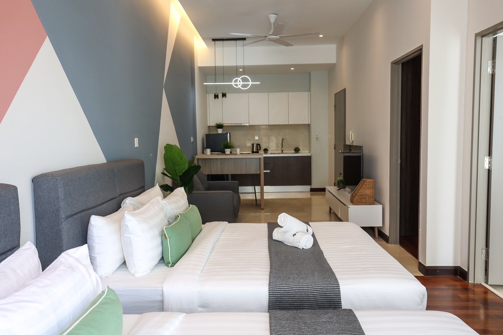 A modern hotel room with a large bed, a desk, and a kitchenette.