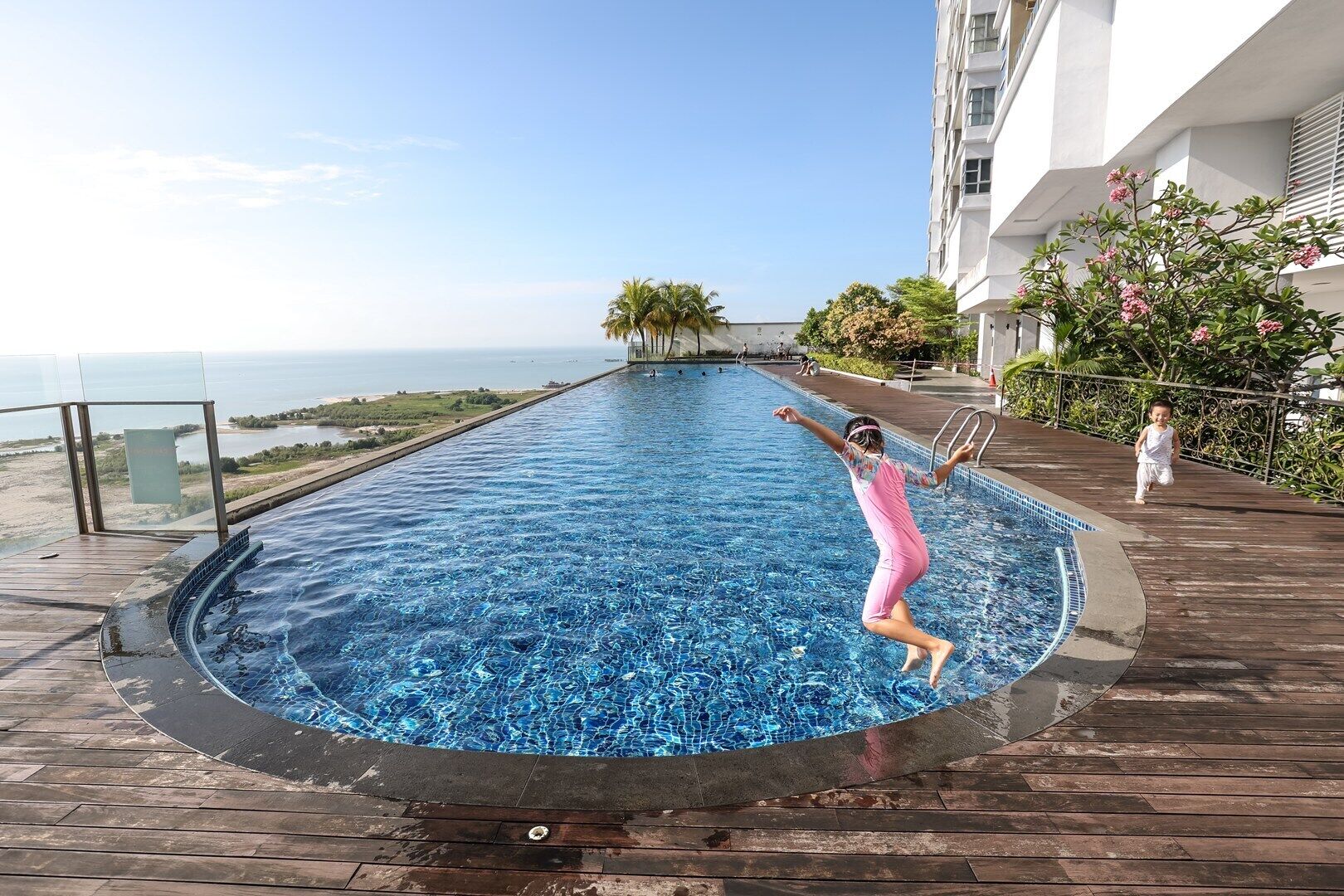 A pool with a view of the sea, surrounded by a wooden deck and a building.