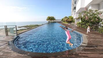 A pool with a view of the sea, surrounded by a wooden deck and a building.