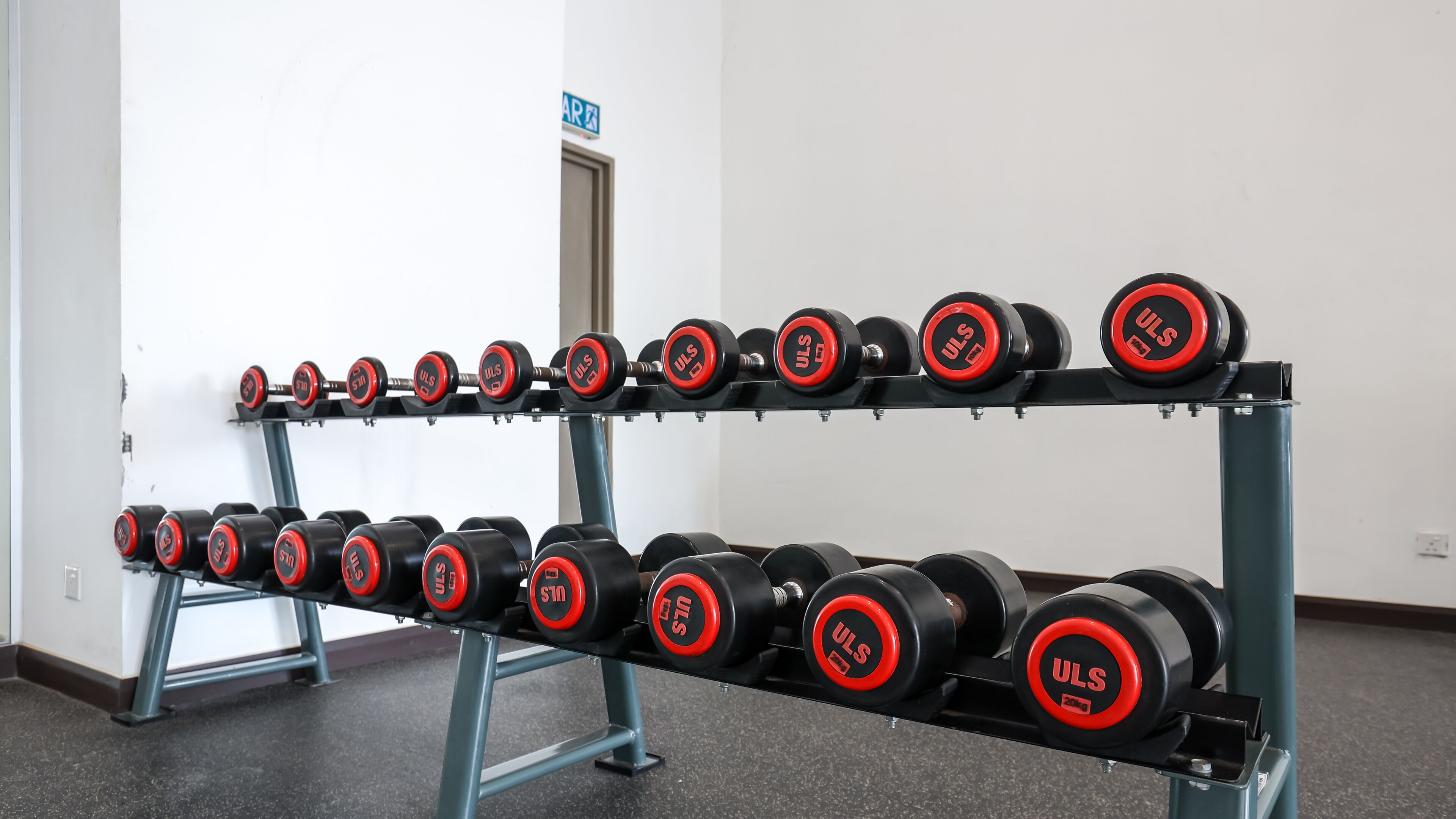 Banco de pesas con varios juegos de mancuernas de la marca ULS.