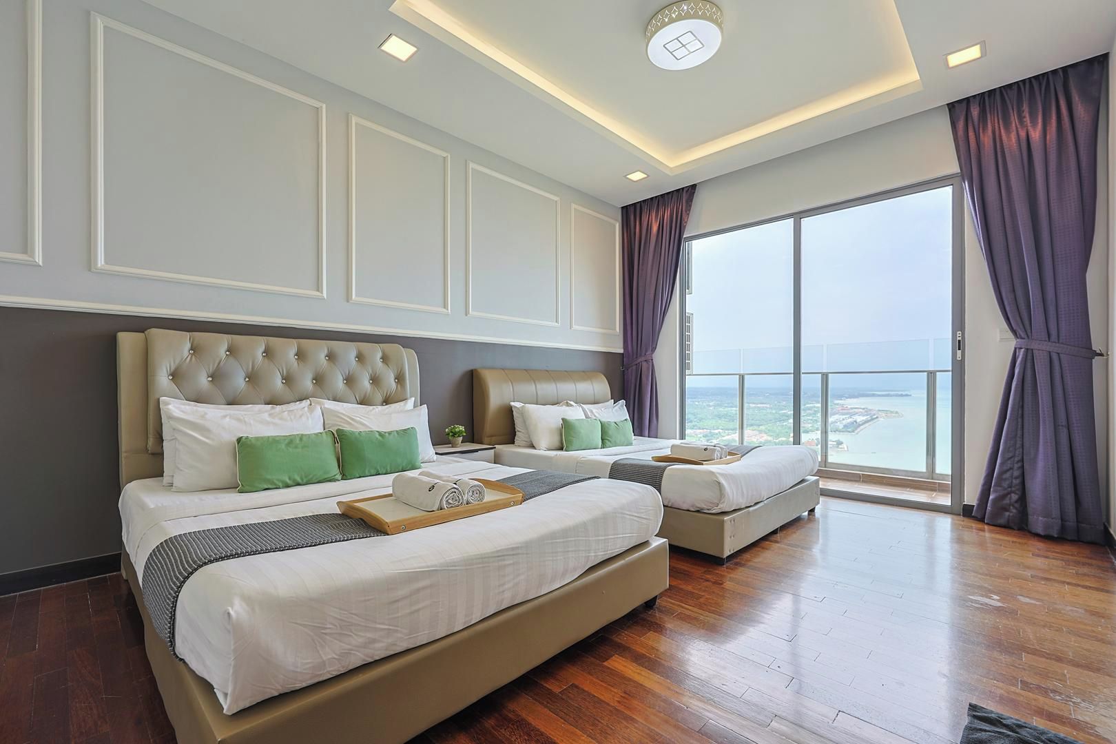 A hotel room with a large bed, two smaller beds, a view of the sea, and a balcony.