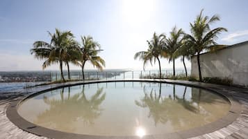 A circular infinity pool with a wooden deck, surrounded by palm trees, overlooking a body of water.
