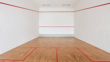 A squash court with white walls and a wooden floor marked with red lines.