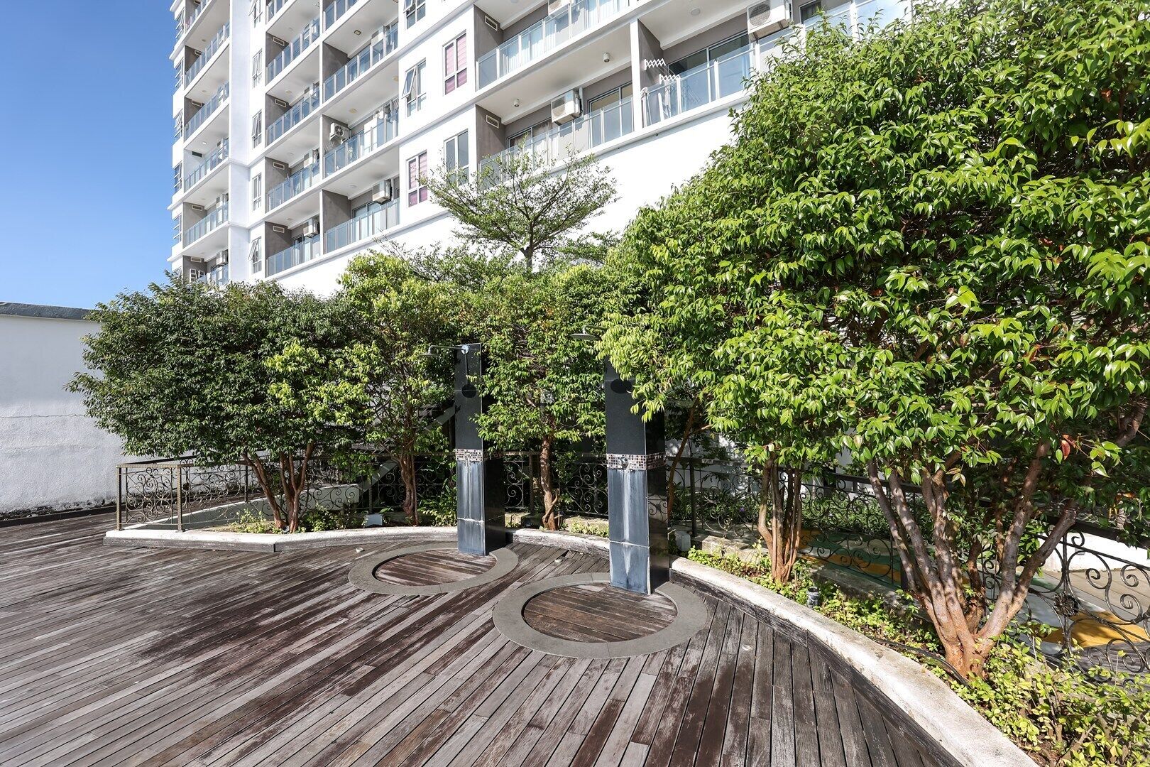 A multi-story residential building with balconies, a wooden deck, and surrounding greenery.
