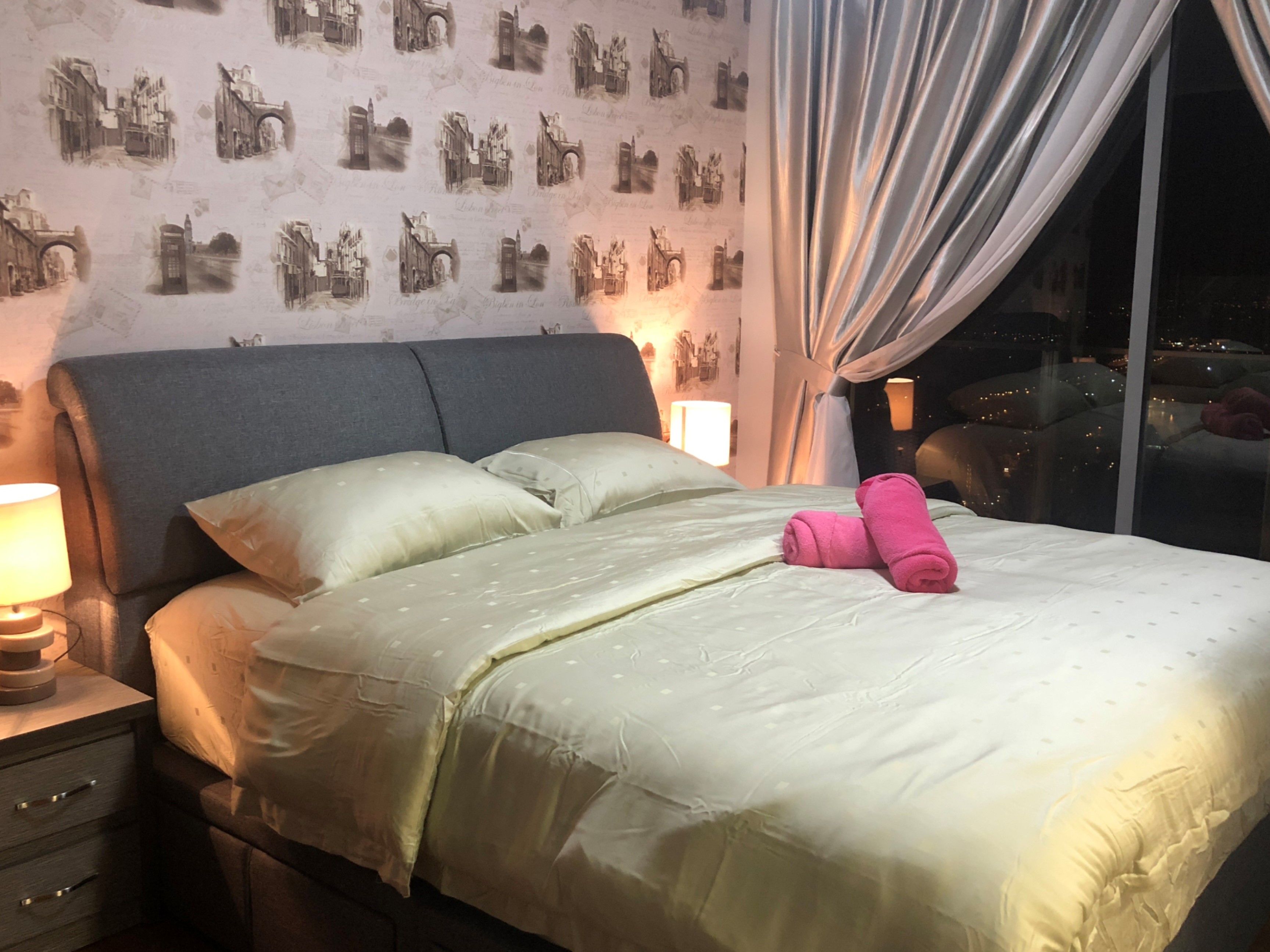 Una habitación de hotel con cama, almohadas, una lámpara de noche y una ventana con cortinas.