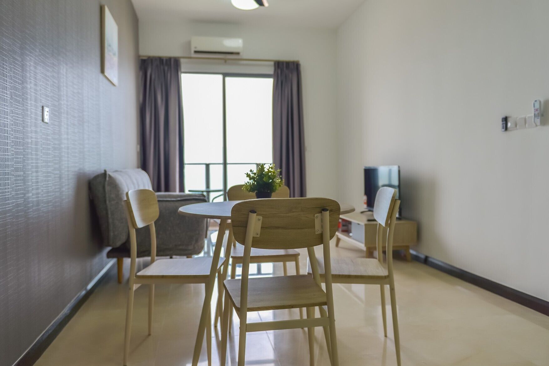 Un salon moderne comprenant une table à manger, des chaises, un canapé, un téléviseur et une grande fenêtre avec des rideaux.