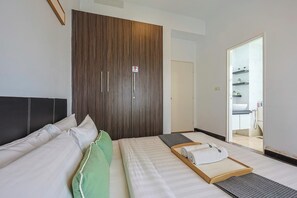 Une chambre d’hôtel avec un lit, une armoire en bois, une salle de bain visible à travers une porte ouverte, et un petit plateau en bois avec des serviettes.