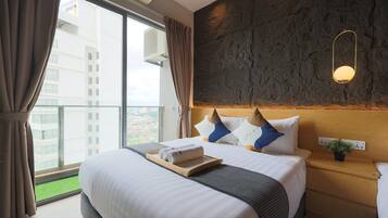 A hotel room with a large bed, a view of the city, a stone accent wall, and a bedside table with a plant.