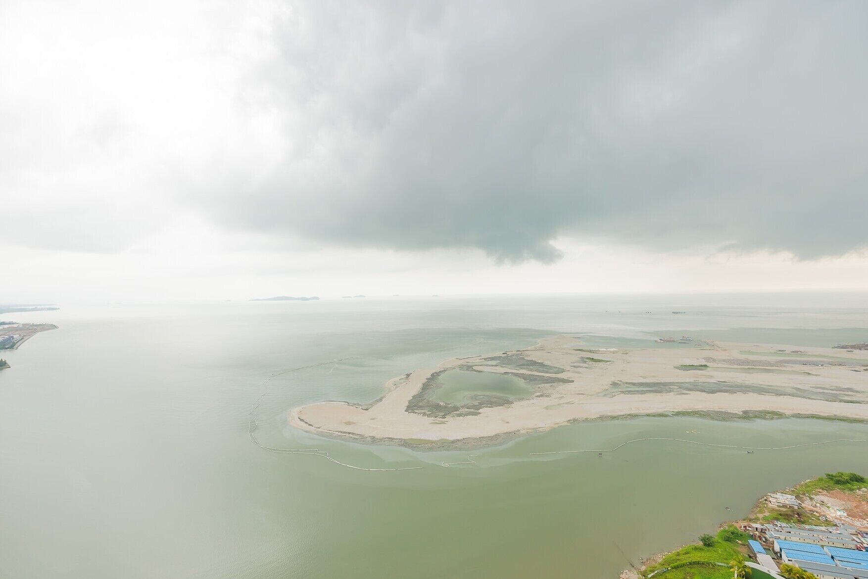 An aerial view of a coastal area with a large body of water, a sandy beach, and a stormy sky.