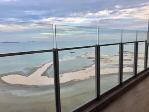 Une vue panoramique depuis une chambre d’hôtel située dans un immeuble de grande hauteur, avec de grandes fenêtres donnant sur un paysage côtier.