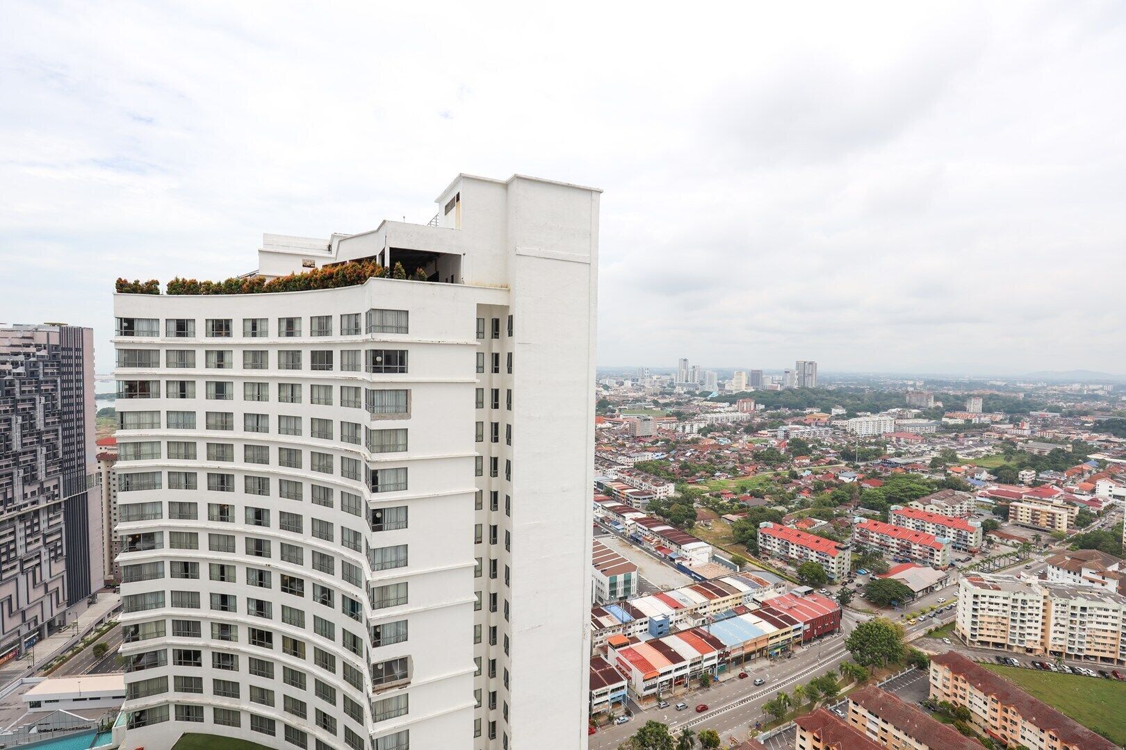 Een hoog gebouw met meerdere balkons, een uitzicht op een stadsbeeld met diverse gebouwen en een heldere lucht.