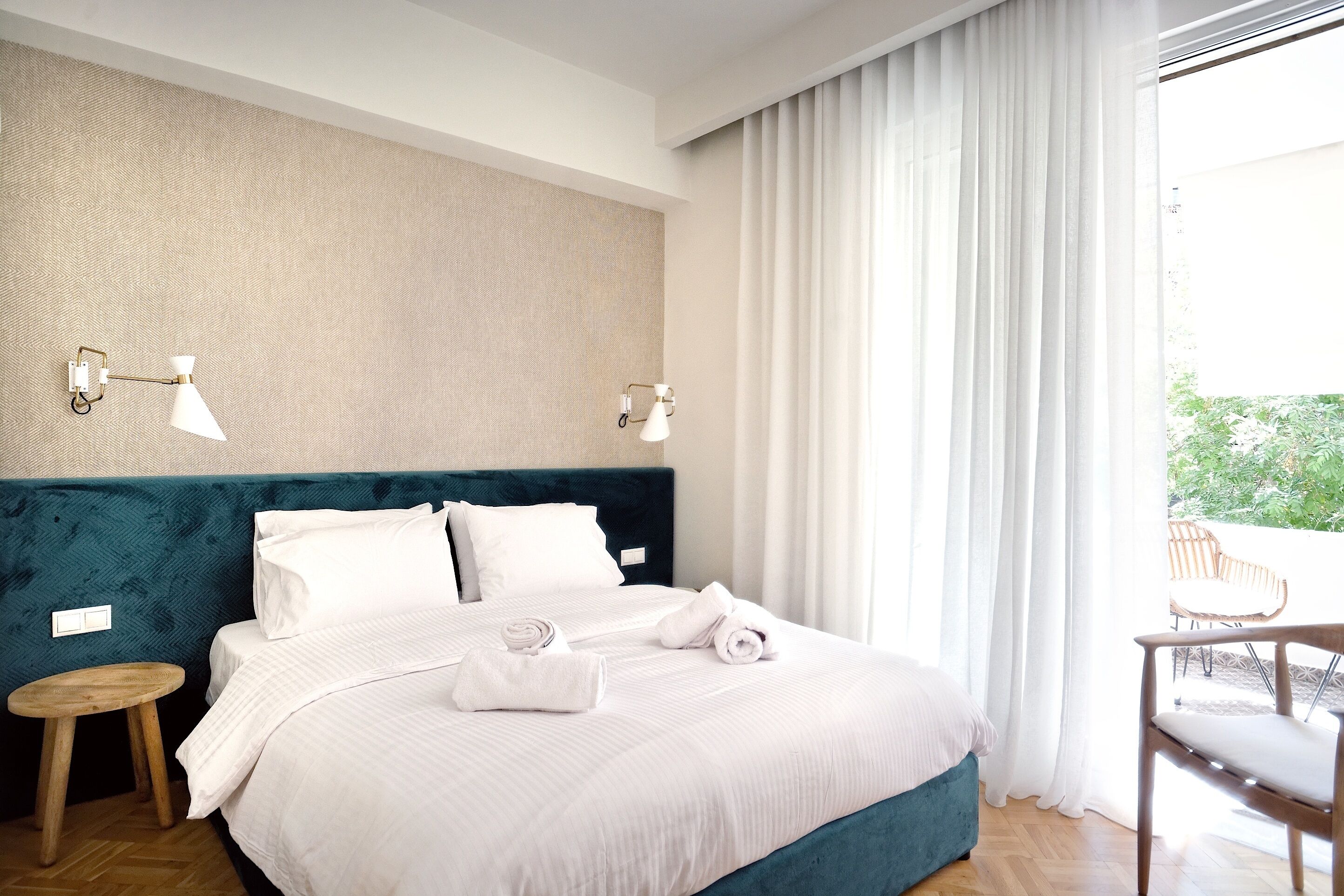 A neatly made bed with white linens, a teal upholstered headboard, and two wall-mounted lamps.