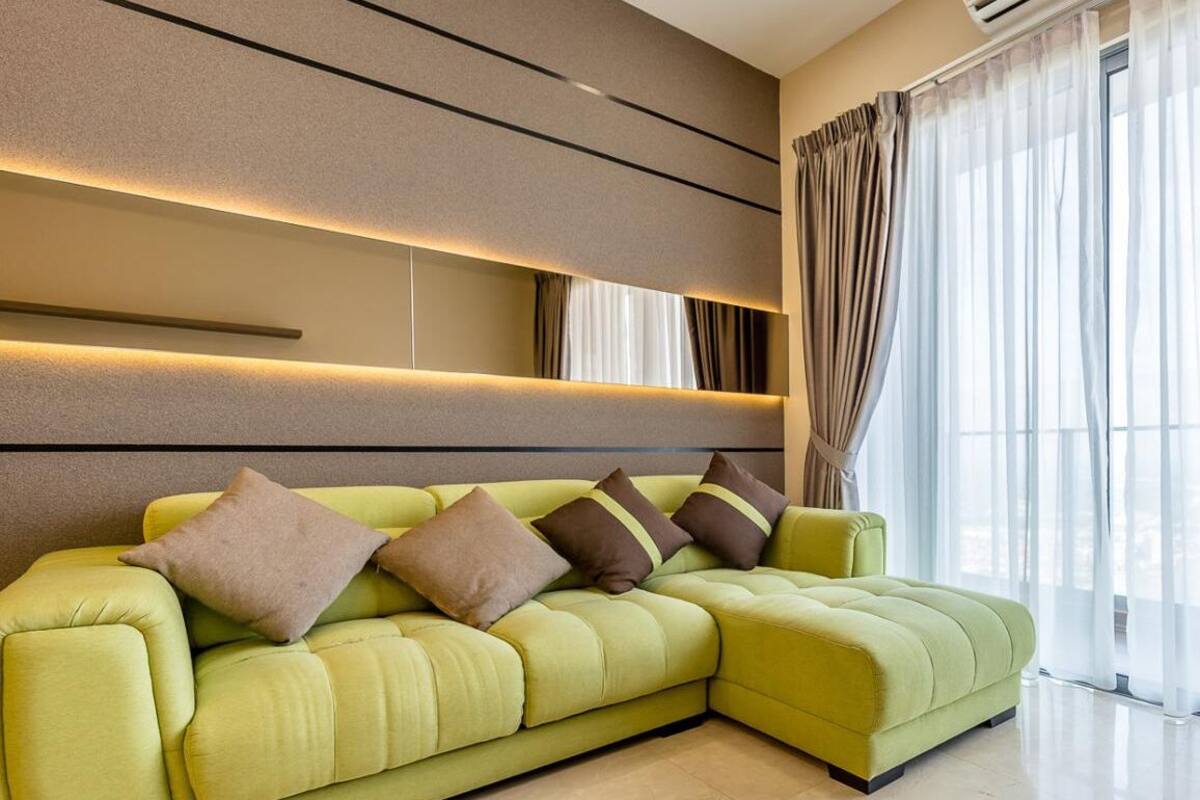 A modern living room with a green sectional sofa, a wall-mounted air conditioning unit, and large windows with sheer curtains.