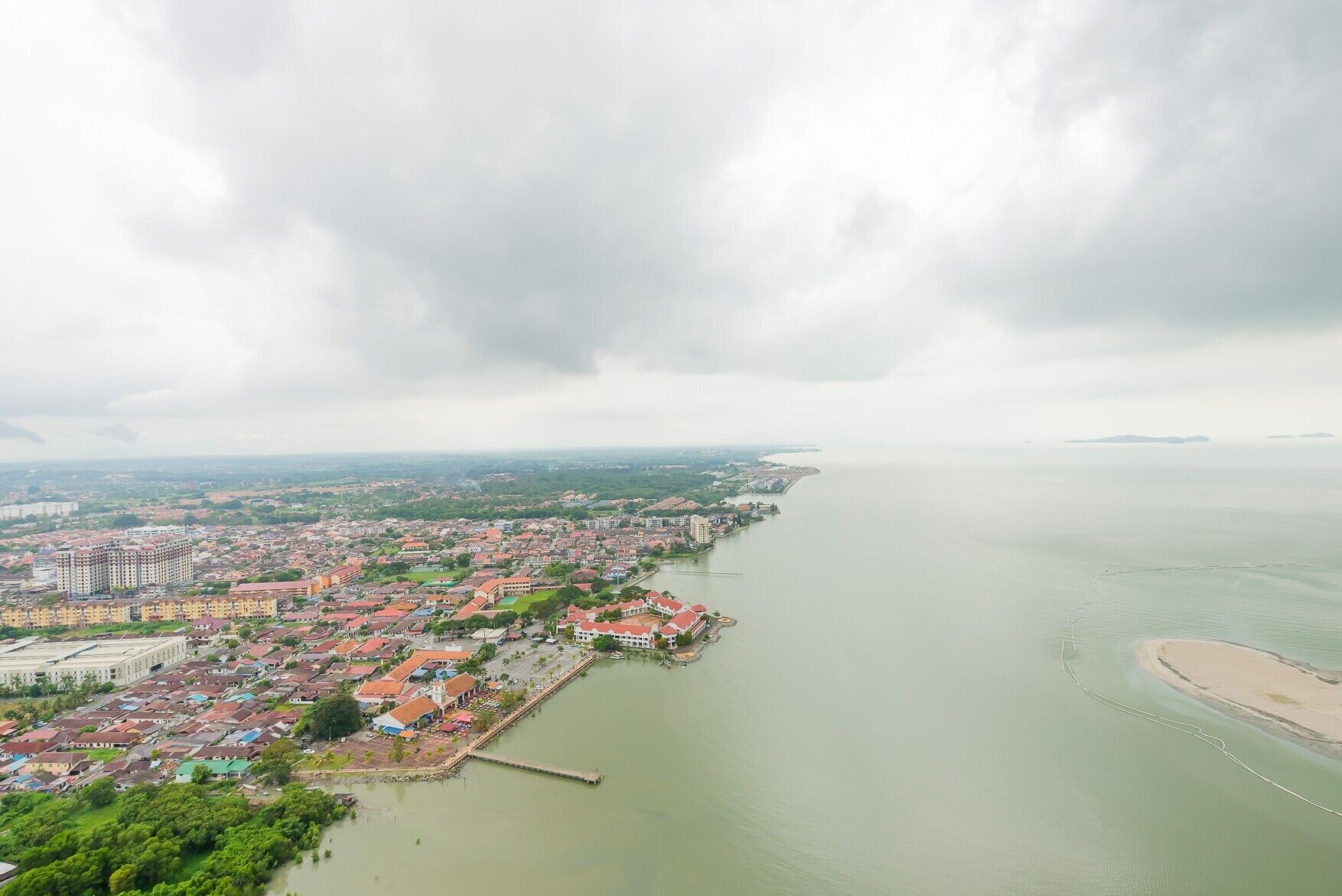 Un paisaje urbano costero con edificios residenciales densos, un puerto deportivo y una isla distante.