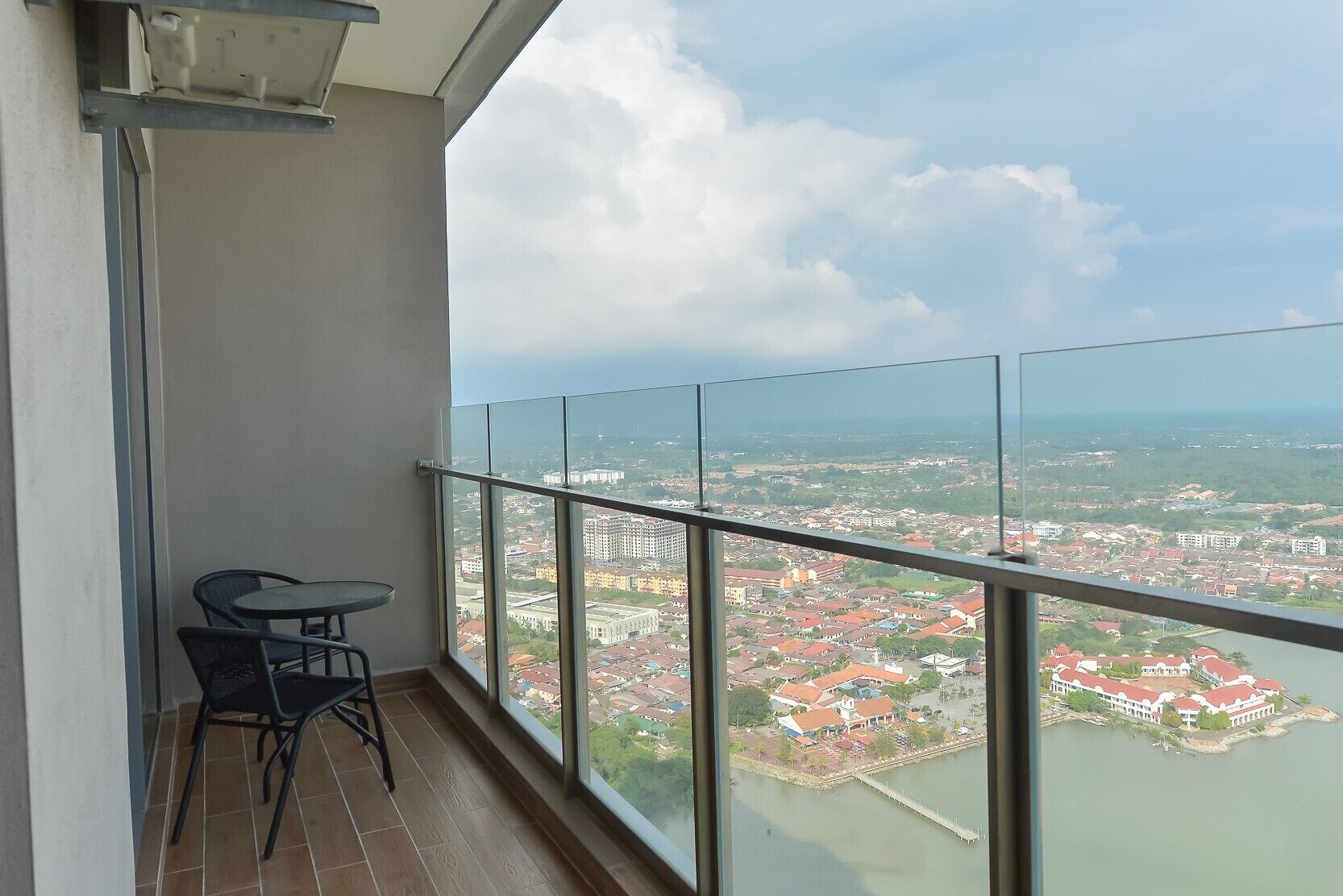 A balcony with a table and chairs, overlooking a cityscape with buildings and a river.