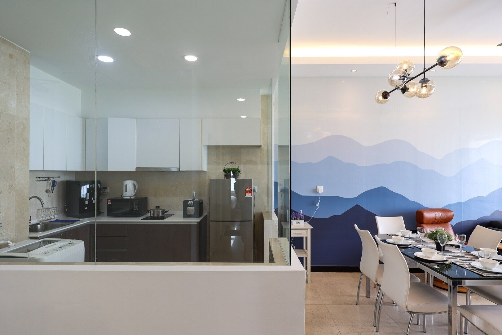 Una cocina moderna con comedor, que incluye un panel de vidrio, electrodomésticos de acero inoxidable y un mural temático de montañas.