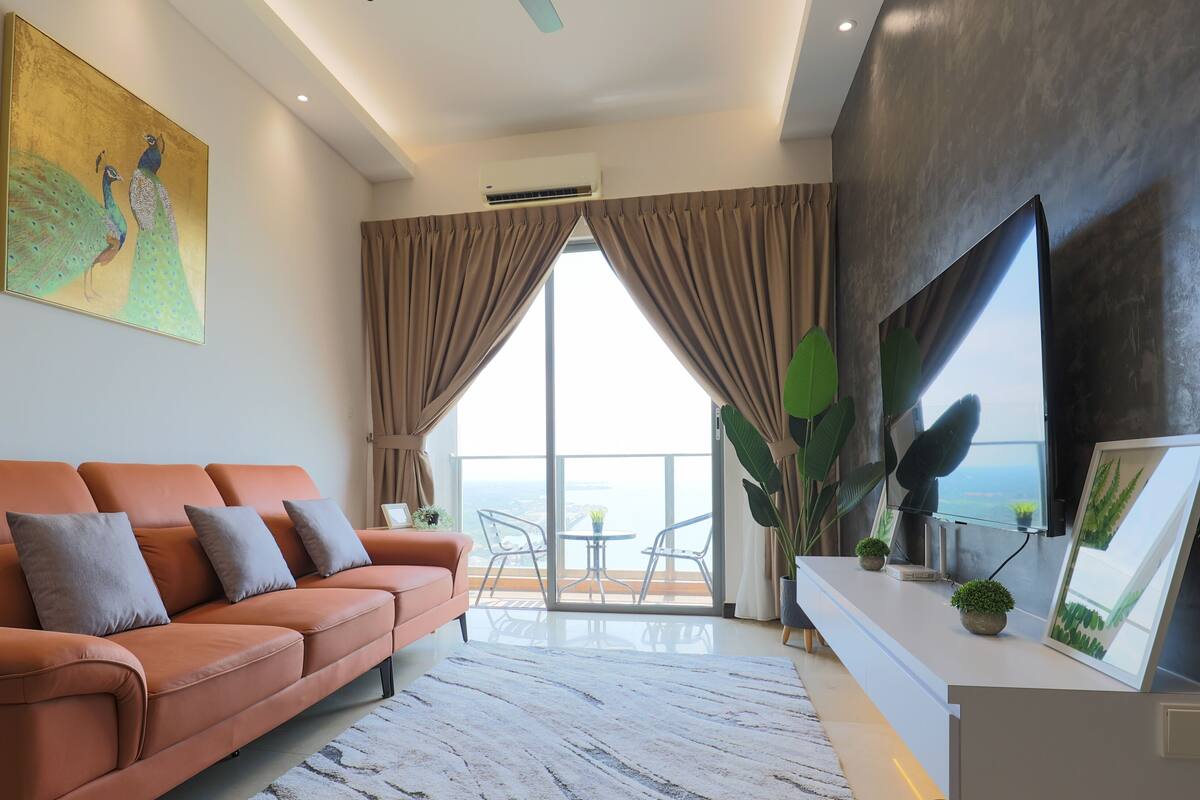 A modern living room with a sofa, a large painting, and a view of the sea through floor-to-ceiling windows.