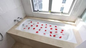 Un baño con bañera, azulejos blancos, una ventana con plantas y el logotipo de iHousing a la vista.