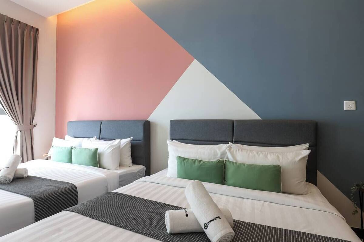 A hotel room with two beds, each with a headboard, white bedding, and green pillows.