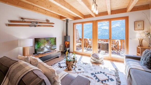 En hyggelig stue med pejs, fjernsyn og en balkon med udsigt til bjergene.