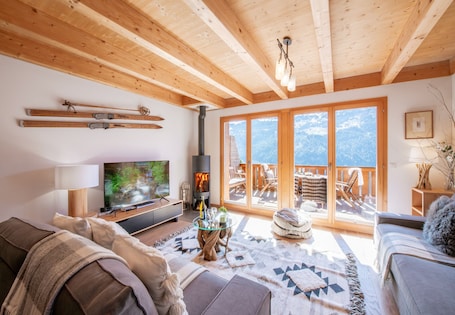 A cozy living room with a fireplace, a television, and a balcony with a view of the mountains.