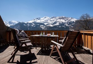 A wooden deck with a table and chairs, overlooking a snow-covered mountain range.
