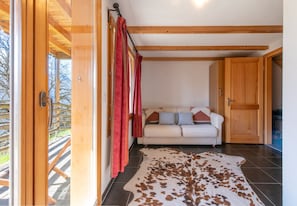 A room with a sofa, wooden beams, a door, and a view through a glass door.