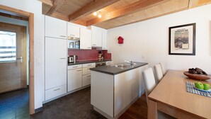 Et moderne køkken med hvide skabe, træloft og et spiseområde med bord og stole.