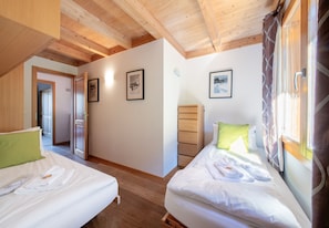 Ein Schlafzimmer mit zwei Betten, Holzbalken an der Decke, einem Holzschrank und gerahmten Bildern an den Wänden.