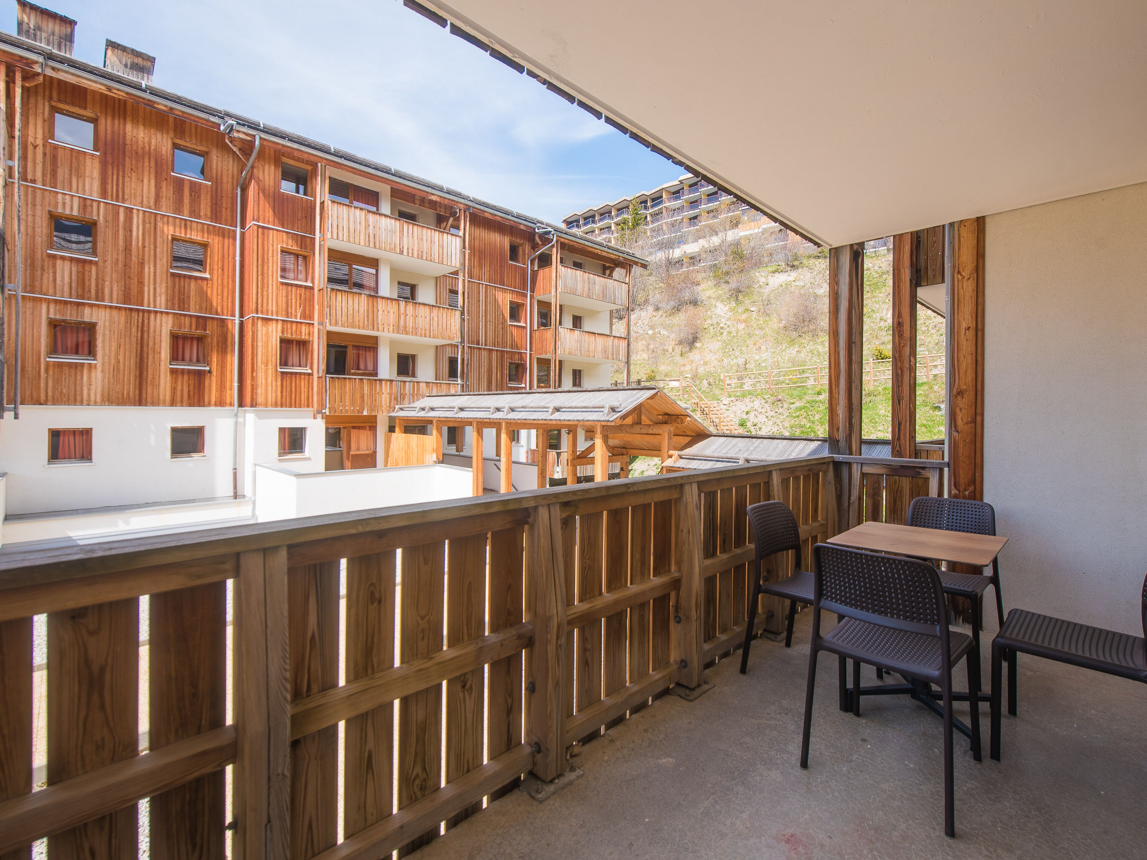 A balcony with wooden railings, a table, and two chairs.