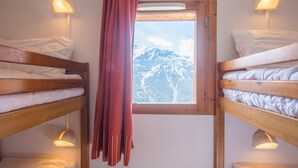 Een kamer met drie stapelbedden, een raam met uitzicht op besneeuwde bergen, en twee wandlampen.