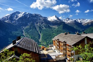Un chalet de montagne composé de plusieurs bâtiments en bois, une piste de ski et, en arrière-plan, des sommets enneigés.