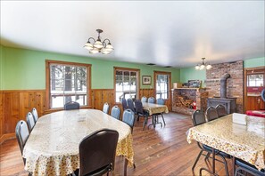 A dining area with a large table and chairs, wooden walls, and a brick fireplace.
