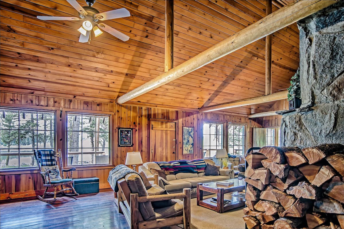 L’intérieur chaleureux d’un chalet avec des murs en bois, une cheminée, un fauteuil à bascule et un canapé.