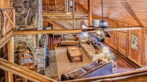 A spacious loft-style room with a stone wall, wooden beams, a staircase, a sofa set, a coffee table, and a hanging light fixture. - Diamond Belle Guest Ranch (Wauconda)
