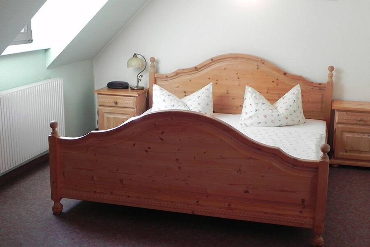 Uma cama de madeira com teto inclinado e uma mesa de cabeceira com abajur.