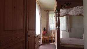Une chambre à coucher avec un lit à baldaquin en bois, une commode en bois et une petite table avec des chaises.