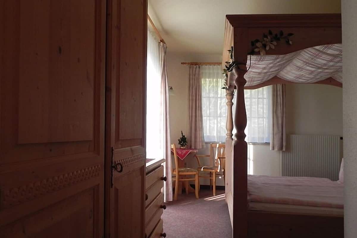 Quarto com uma cama de dossel de madeira, cômoda de madeira e uma pequena mesa com cadeiras.