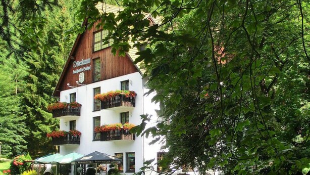 Un bâtiment traditionnel en bois, doté de nombreux balcons ornés de fleurs et entouré d’une végétation luxuriante.