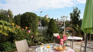 Una terrazza esterna con un tavolo apparecchiato per la colazione, immersa nel verde e tra fiori.
