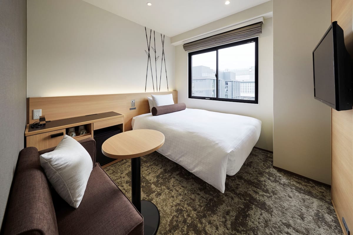 A modern hotel room with a large bed, a small desk, a round table, a sofa, and a TV.
