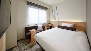 A hotel room with a large bed, a sofa, a desk, and a window with blinds.