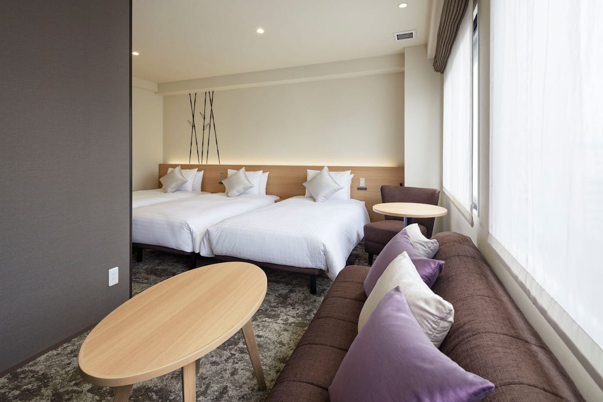 A hotel room with two beds, a sofa, a small table, and a large window.