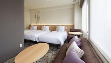 A hotel room with two beds, a sofa, a small table, and a large window.